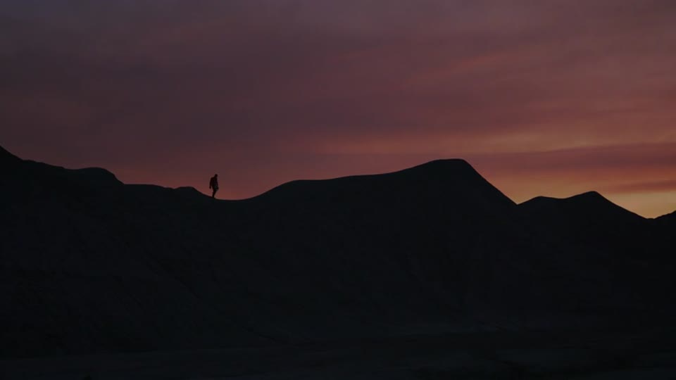 Night falls. He walks on along the ridge, a small silhouette