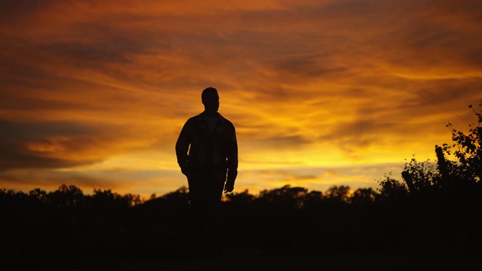He stands in silhouette under the burning evening sky and watches the day go