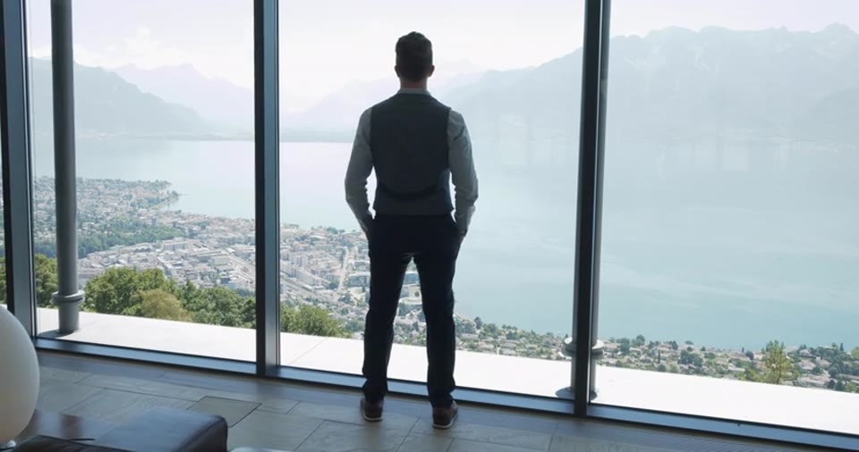 He stands at the glass of his house, in silhouette. Everything below him is his