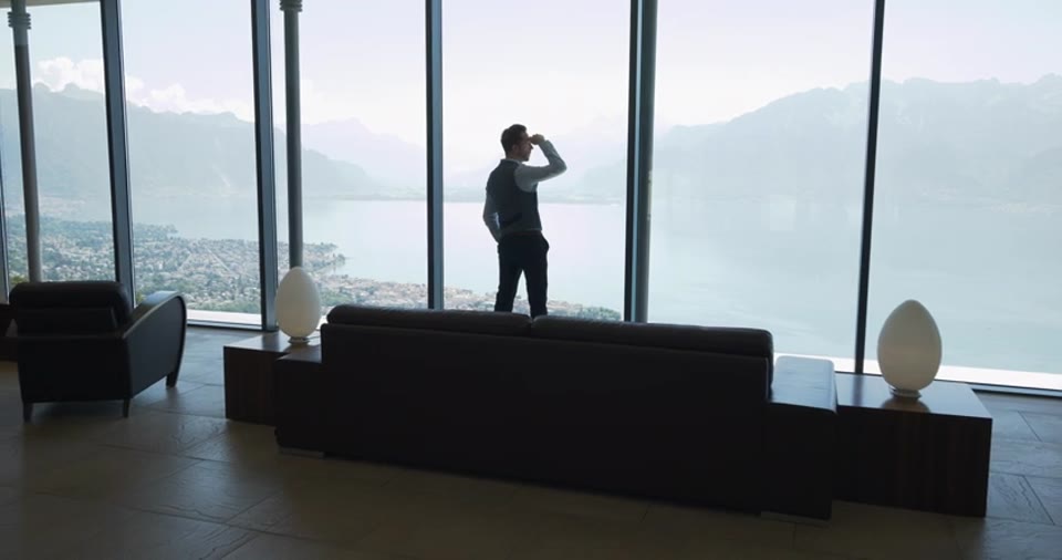 The same shot pulls back: the whole house around him, and he looks out over all of it